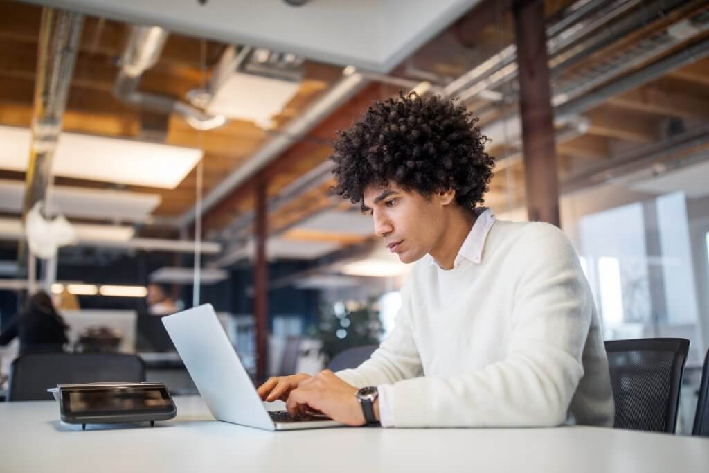 Side view of young businessman using laptop in office. Male professional sitting at conference table working on laptop computer.